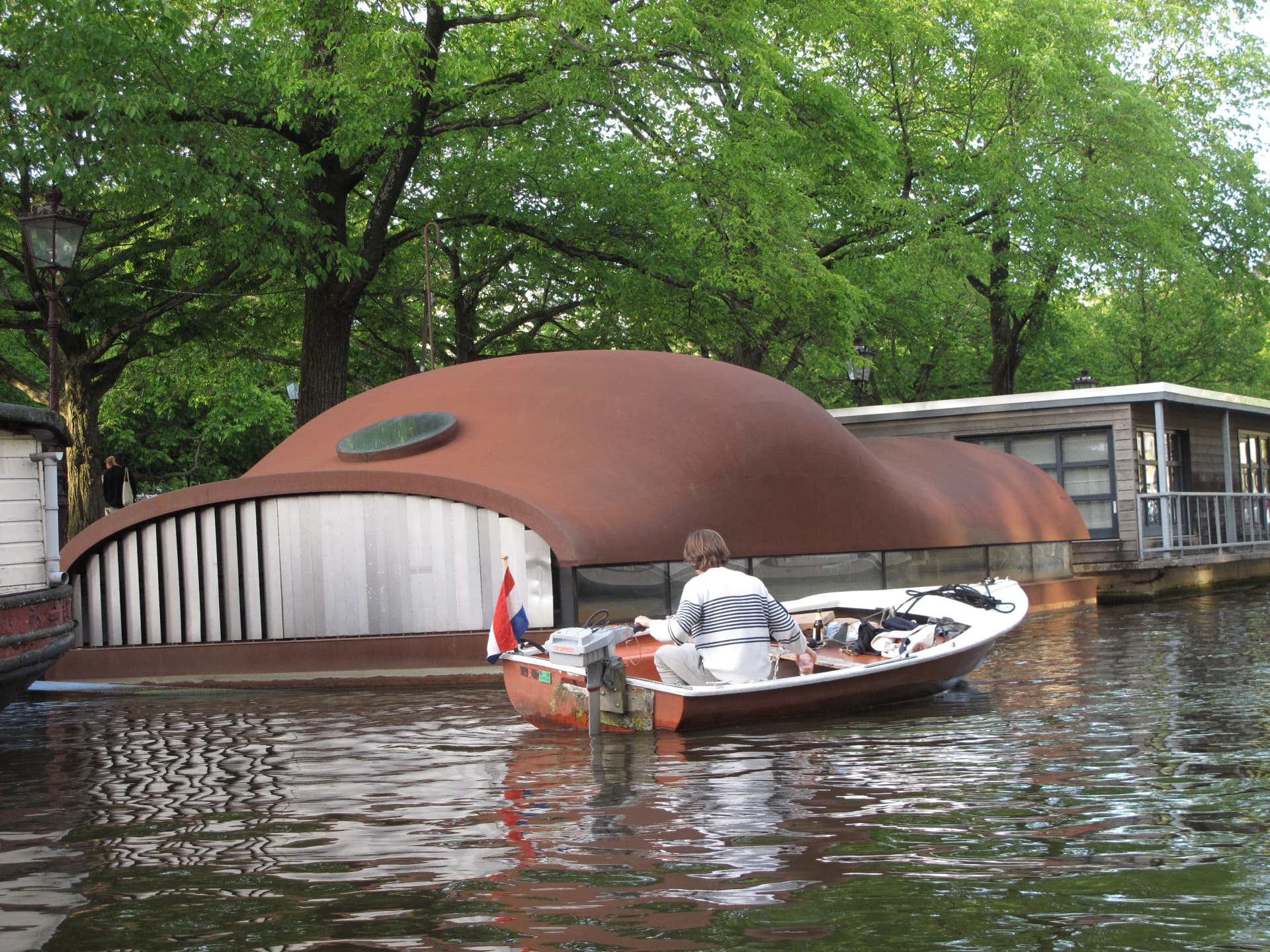 A small boat passing a houseboat with a rounded rust brown roof