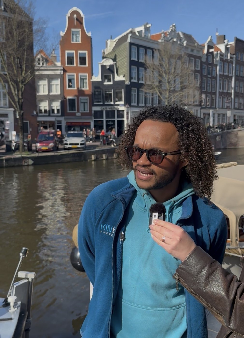 Talking on the quay with a microphone, canal houses behind